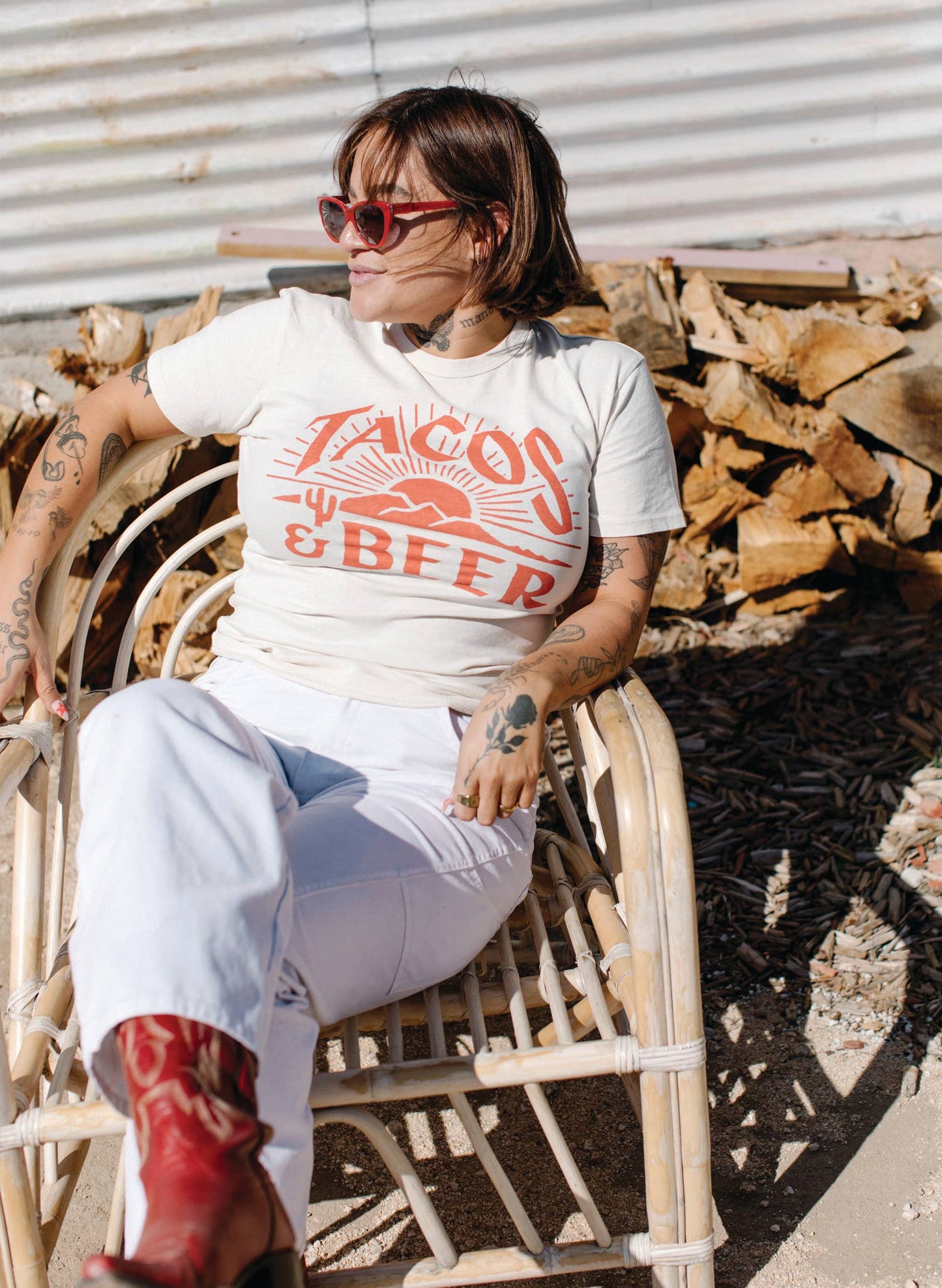 Person wearing a white t-shirt with red text, sitting on a chair with wood behind them.