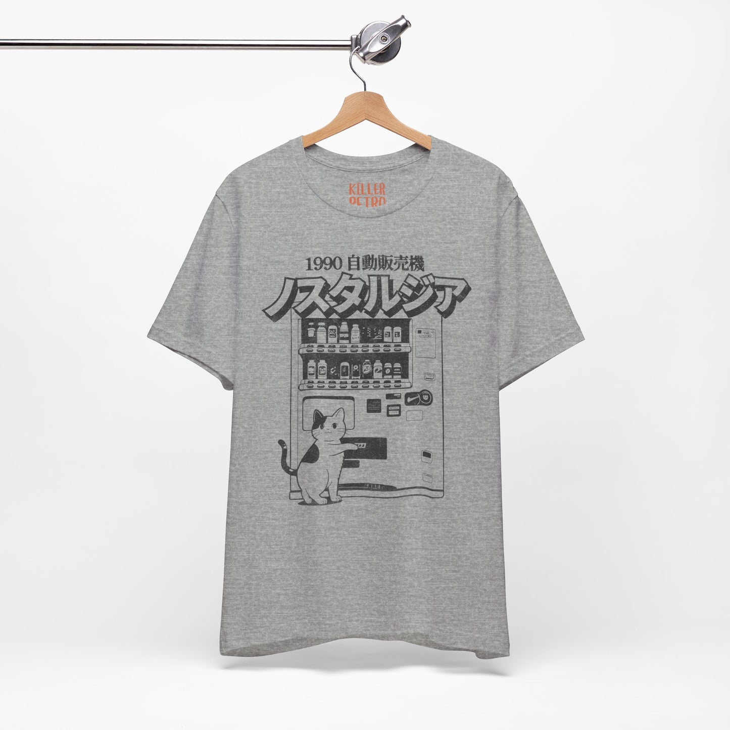 Gray t-shirt with a graphic design of a cat and vending machine on a hanger against a white background