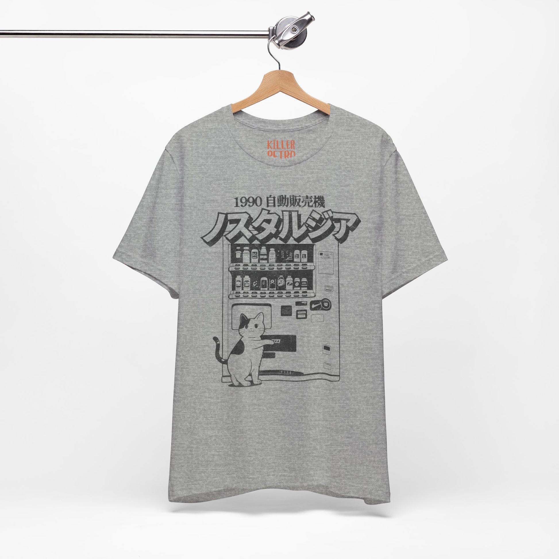 Gray t-shirt with a graphic design of a cat and vending machine on a hanger against a white background