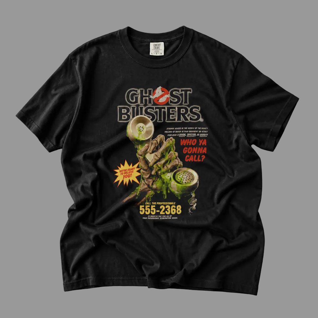 A black short-sleeve Ghostbusters graphic t-shirt laid flat on a textured gray concrete surface. The front of the shirt features a detailed graphic print with the Ghostbusters logo, a ghost, a green potion bottle, and red and yellow text.
