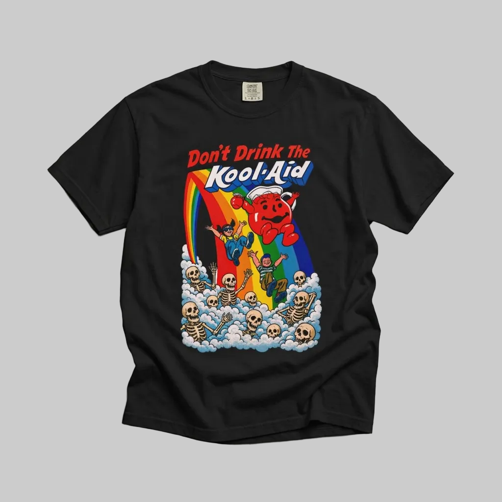 A black short-sleeve t-shirt laid flat on a textured gray concrete background, featuring a colorful retro graphic of the Kool-Aid brand with a red character, rainbow, skeletons, and the text 'Don't Drink The Kool-Aid'.