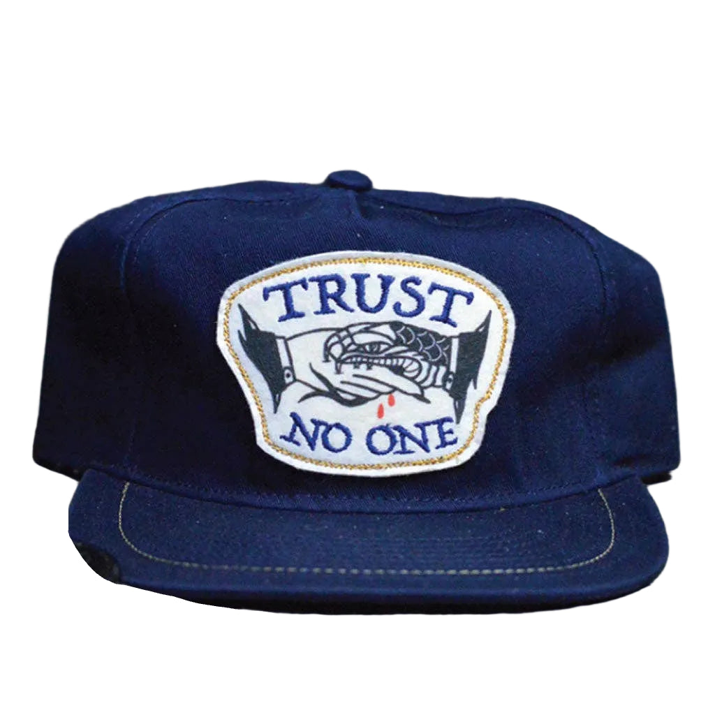 Blue cap with 'Trust No One' patch on a wooden surface