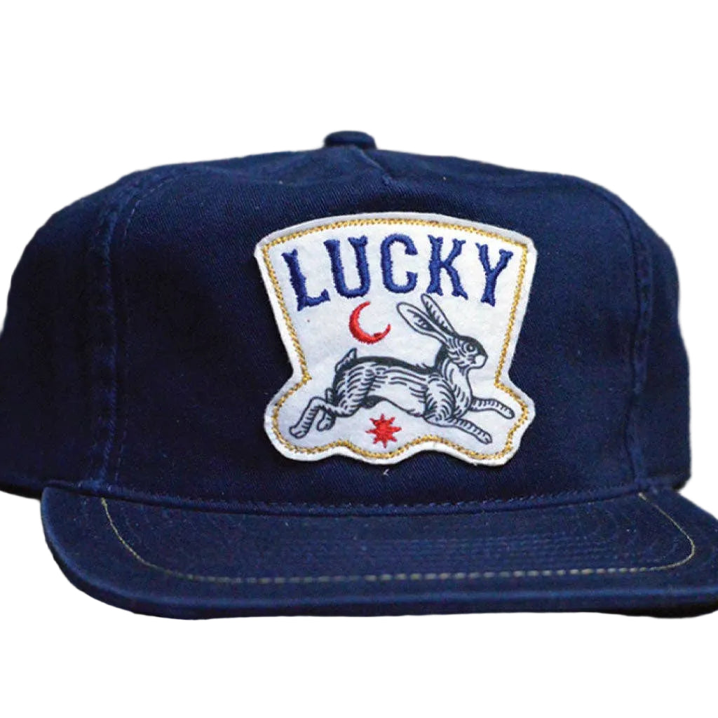 Blue cap with 'LUCKY' patch featuring a rabbit design on a wooden surface with playing cards.
