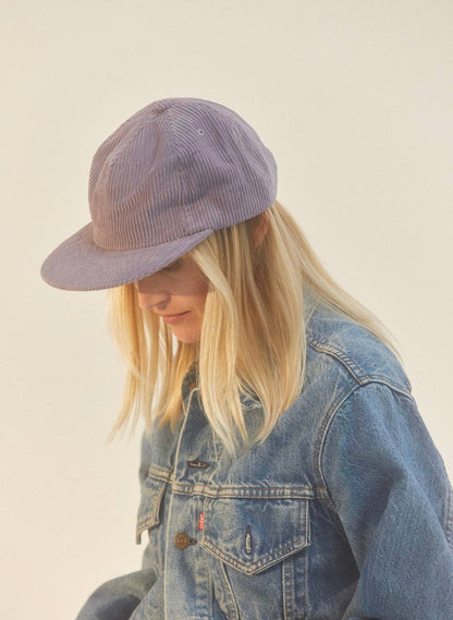Person wearing a denim jacket and purple cap on a plain background