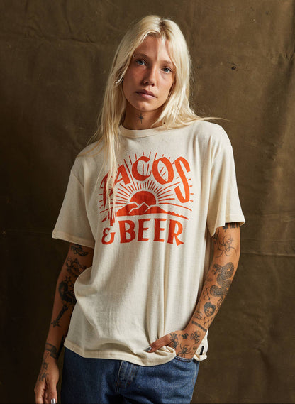 Person wearing a t-shirt with 'Tacos & Beer' text against a brown background