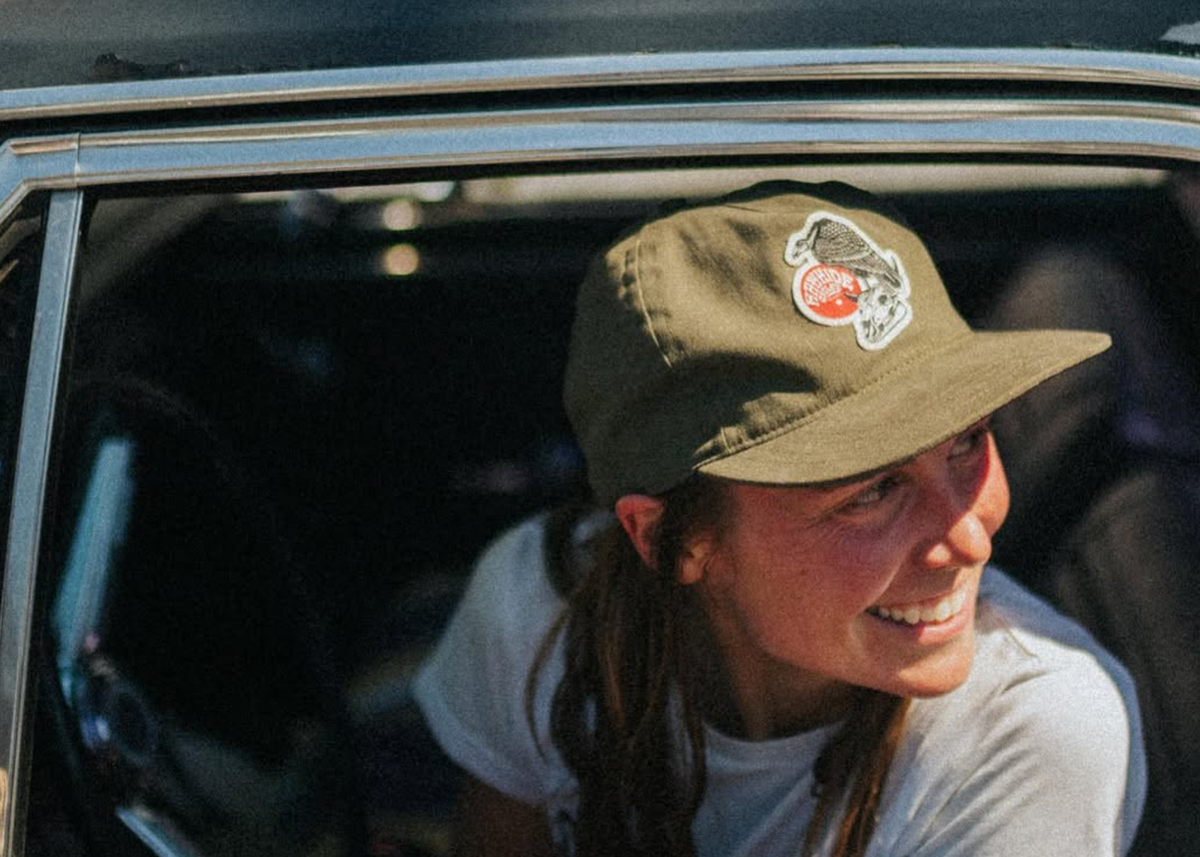 Person wearing a cap with a logo, sitting inside a vehicle.