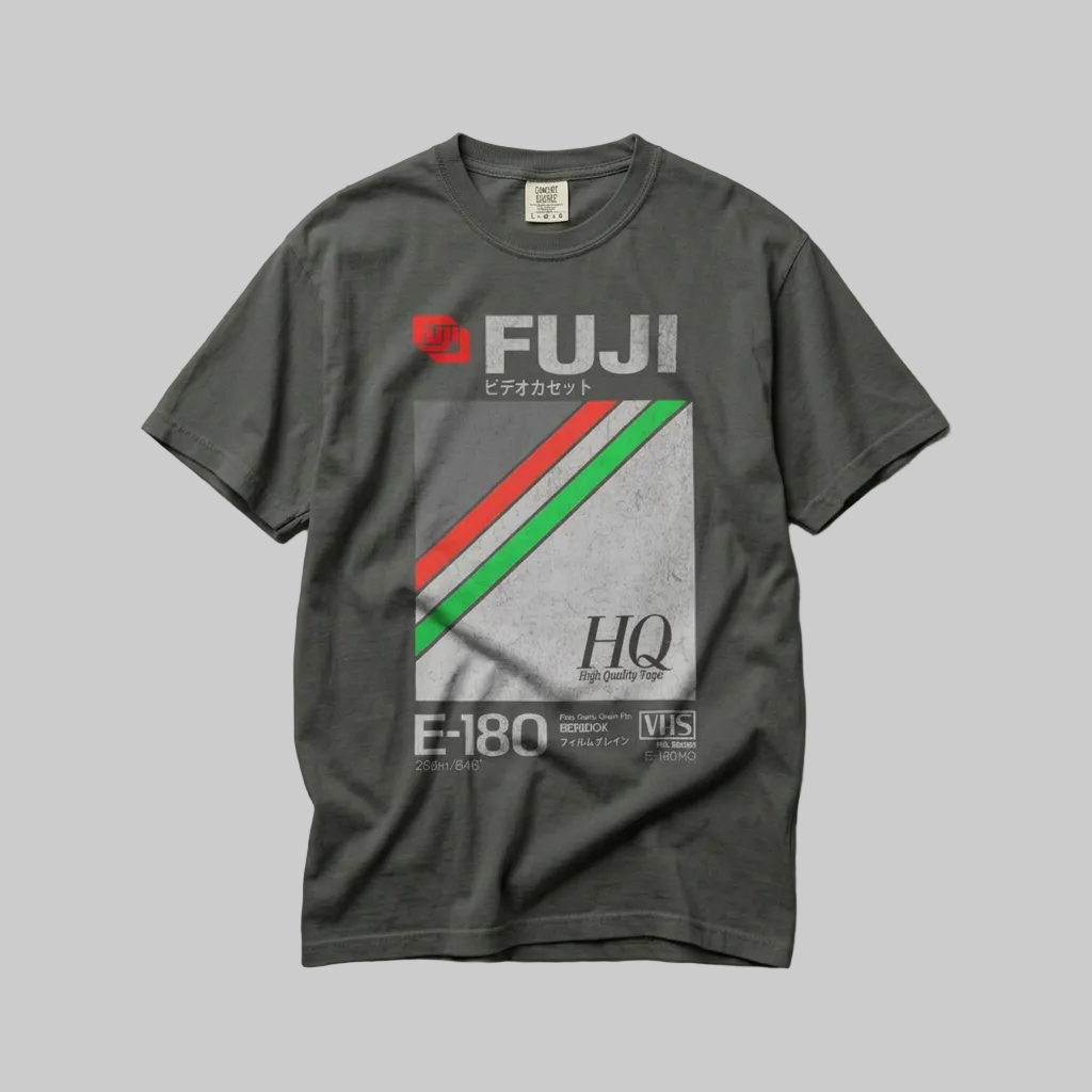 A dark gray graphic t-shirt featuring the FUJI brand logo and a red, green, and white striped design, laid flat on a textured gray concrete background.